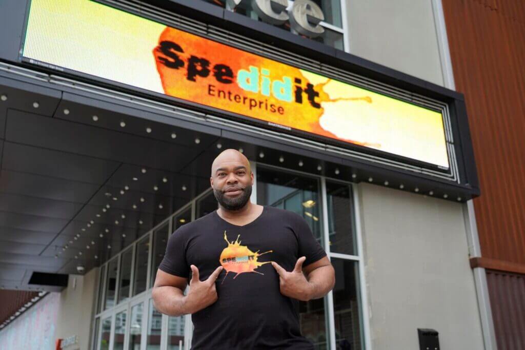Host standing under the Spedidit Enterprise sign at the event entrance